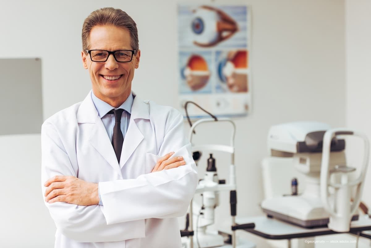 An ophthalmologist standing with his arms crossed and smiling in the office. (Image Credit: AdobeStock/georgerudy)