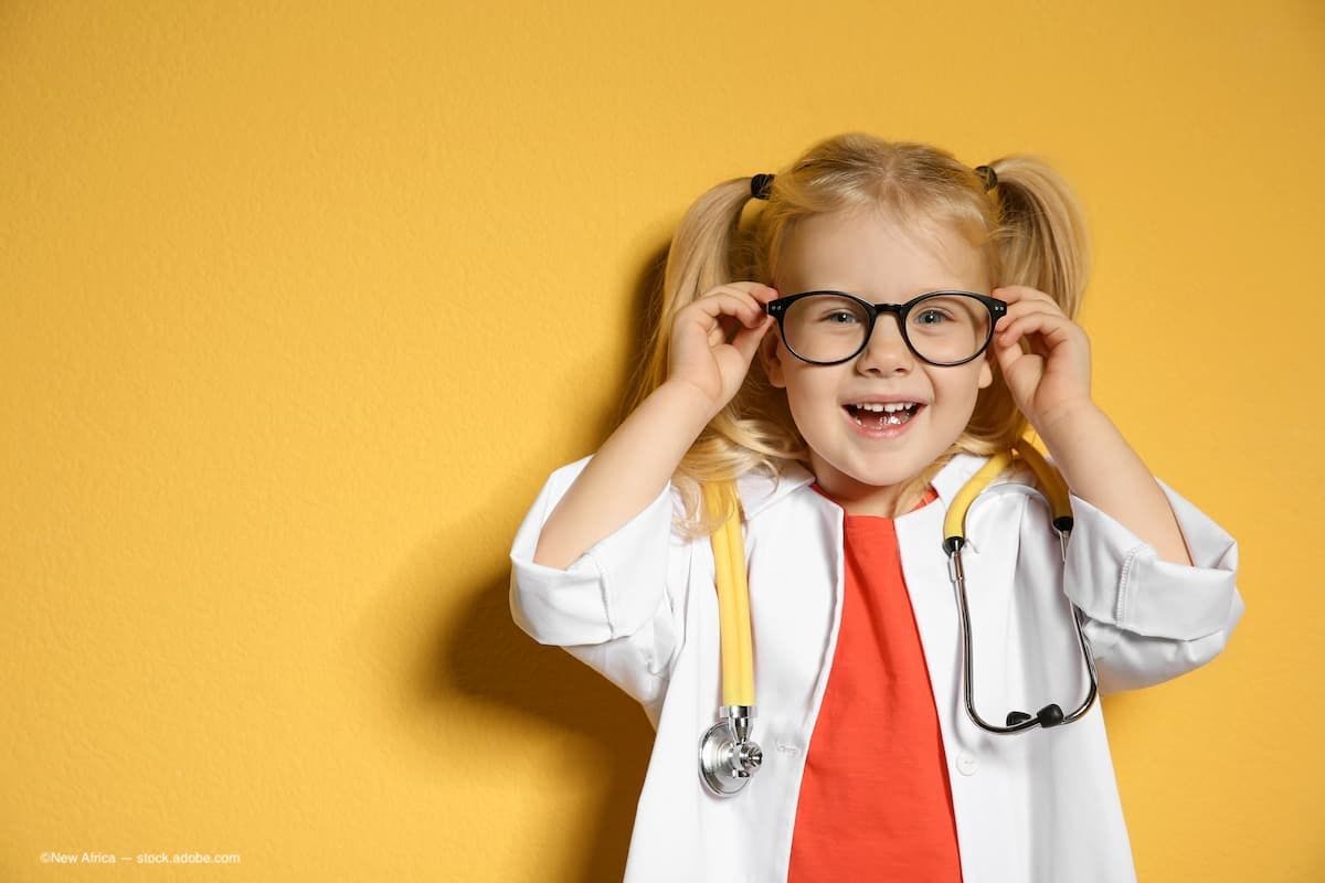 A child wearing a labcoat and glasses, smiling, in front of a yellow background. (Image Credit: AdobeStock/New Africa)