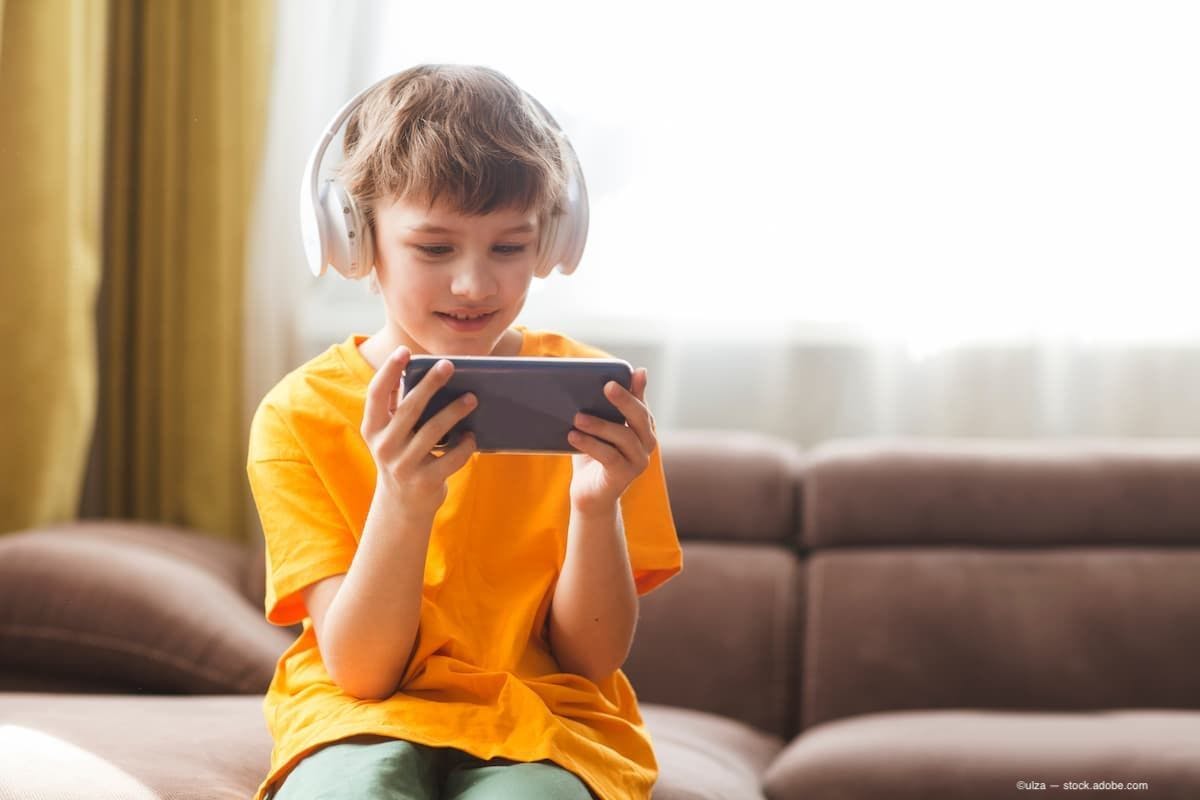 A child on his phone with headphones on smiling. (Image Credit: AdobeStock/ulza)